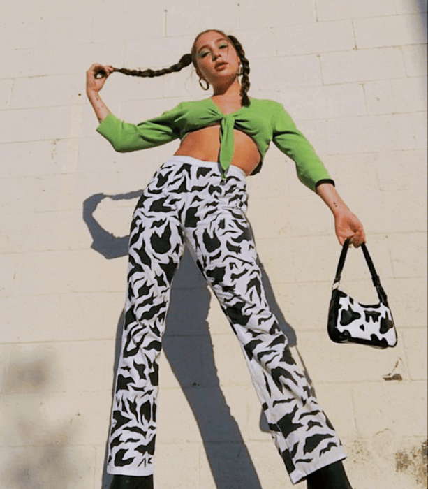 chica de cabello castaño usando una blusa crop top verde con pantalones de cebra holgados, botines negros y bolso de vaquita pequeño