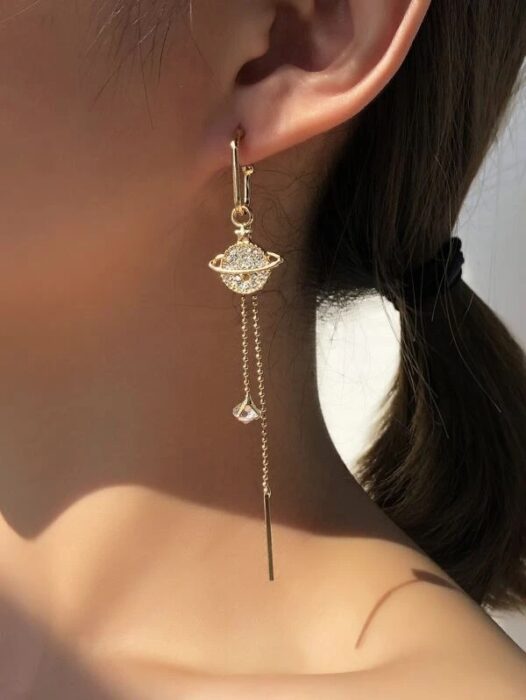 Chica usando unos aretes en forma de planeta con diamantes