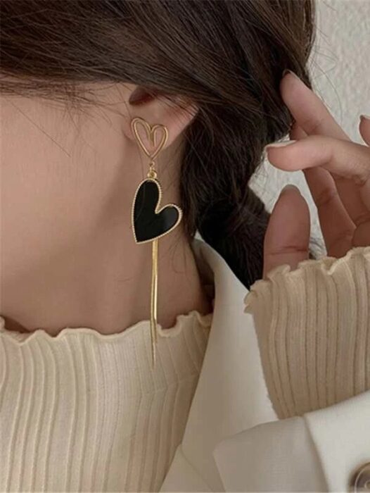 Chica usando unos aretes largos de color negro con dorado en forma de corazón 