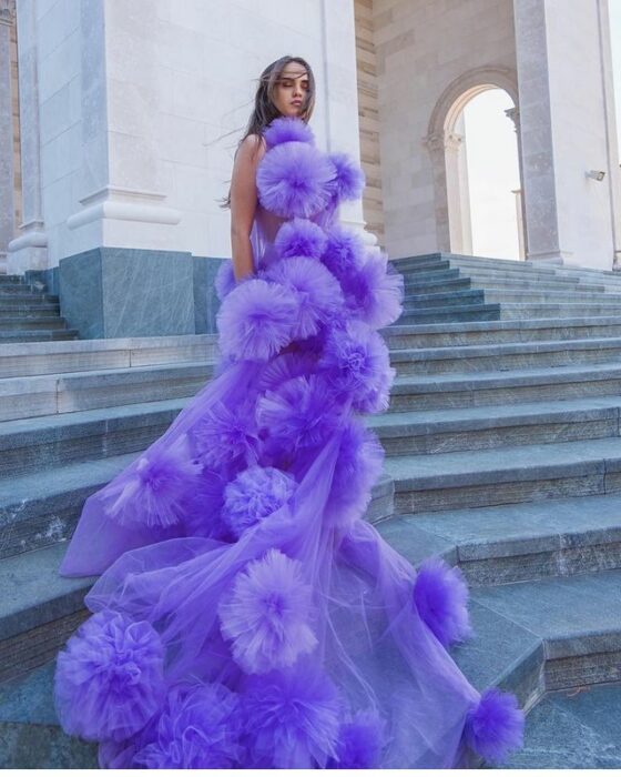 Chica usando un vestido de color morado con pompones grandes 