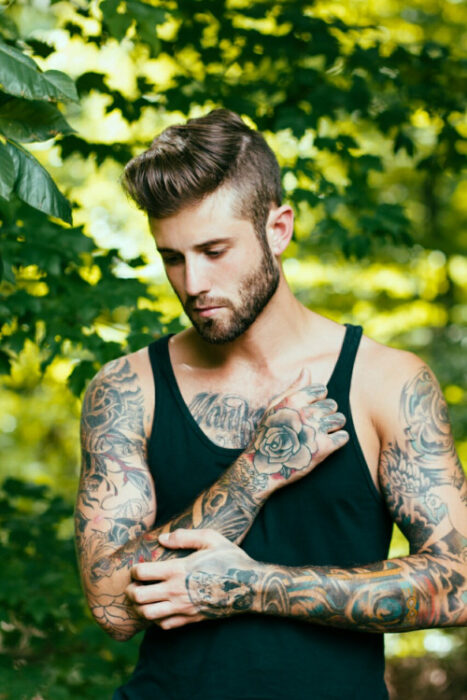 Chico con tatuajes pensando mientras está en un jardín 