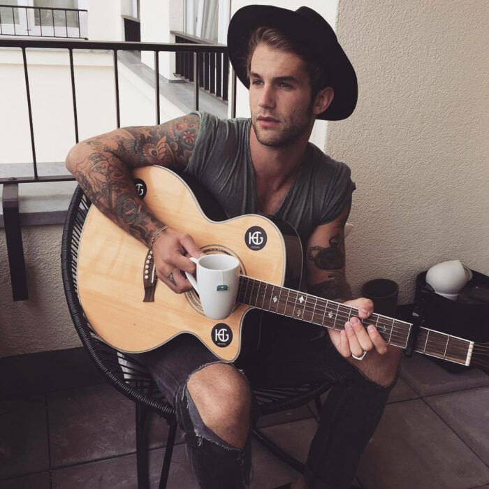 Chico sentado en una silla tomando café y tocando la guitarra 