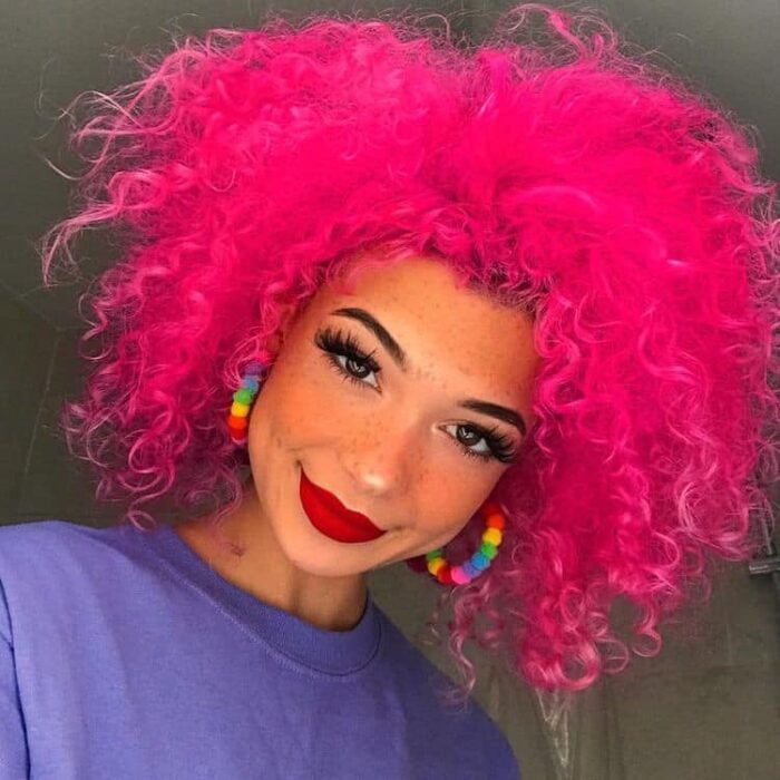 Chica con el cabello rizado y teñido de color rosa fuccia 