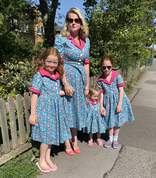 Rosie Chandler y sus hijas usando vestidos similares en tonos azules y rosas 