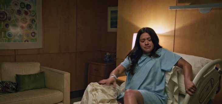 Mujer intentando pararse de una cama de hospital mientras está vestida con una bata 