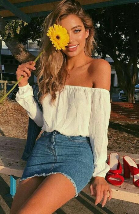 Chica posando para una fotografía mientras sostiene un girasol en sus manos 