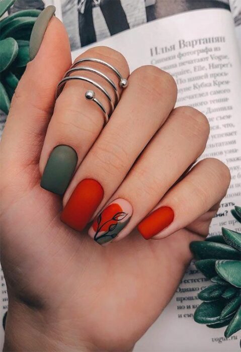 Manicura en tonso rojo y verde, decorado con una hoja en tono negro; Uñas bonitas con diseño de hojitas