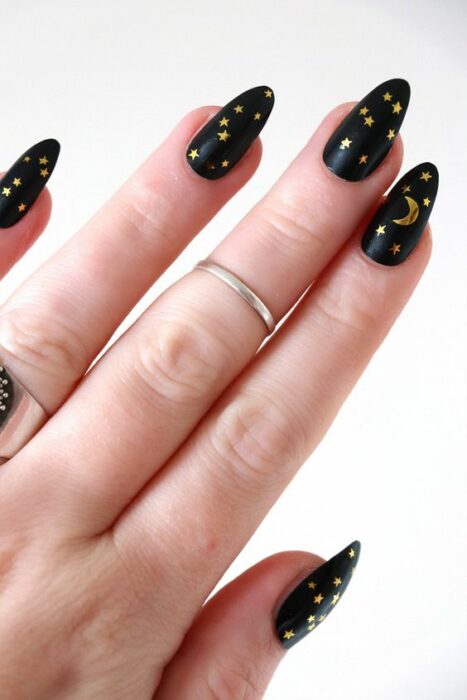 Manicura en tono negro con estampados en oro; Uñas con lunitas que amarás 