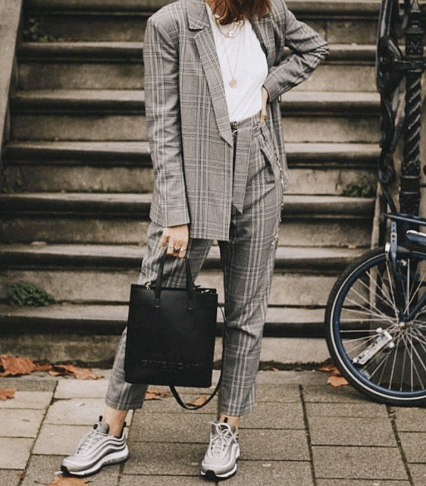 chica con traje gris, camiseta blanca, tenis grises con blanco, bolso negro de cuero