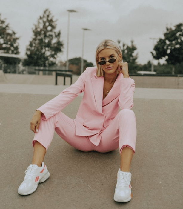 chica de cabello rubio con lentes de sol negros, traje rosa pastel y tenis blancos