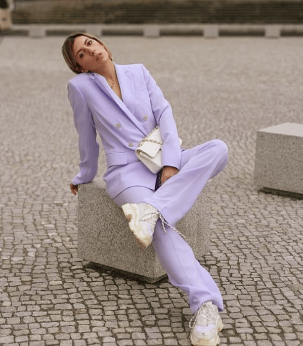 chica de cabello oscuro usando un traje color lila y tenis blancos, bolso blanco de cuero