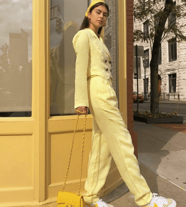 chica de cabello castaño usando un saco blazer amarillo, pantalones de vestir amarillos, bolso de mano amarillo, tenis blancos