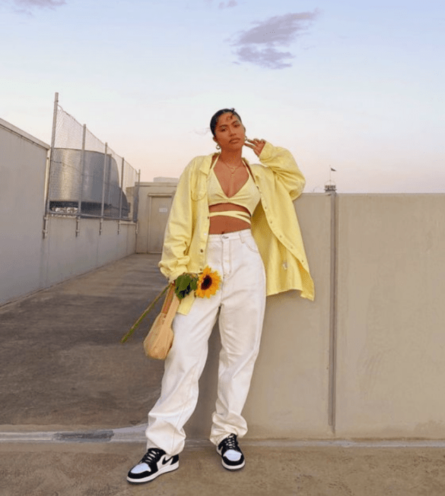 chica morena con crop top de tirantes amarillo pastel, camisa oversized amarillo pastel, pantalones blancos holgados, tenis blancos con negro