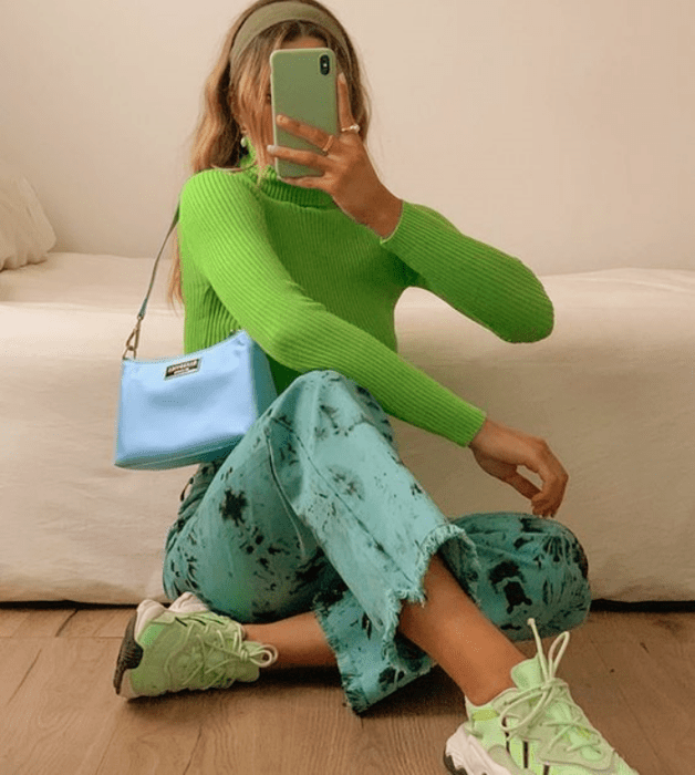 chica rubia con top verde neón de manga larga, pantalones azules, tenis deportivos verde menta, bolso azul celeste de cuero