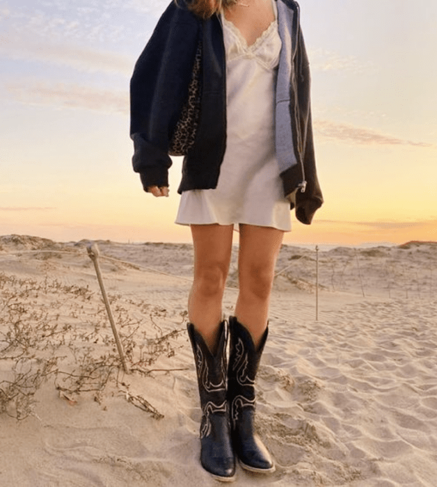 chica con sudadera negra, vestido de satén blanco tipo camisón con encaje, botas de vaquero negras altas