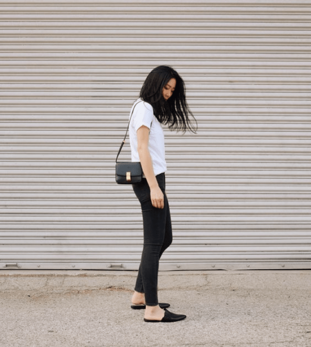 chica de cabello oscuro, playera blanca, jeans negros ajustados, flats negros y bolso de piel negro