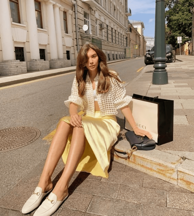 chica de cabello claro usando una blusa blanca de mangas abombadas, falda de satén amarilla, flats blancos de cuero tipo loafers 