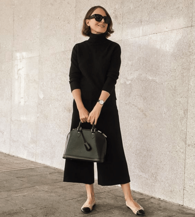 chica de cabello corto castaño usando lentes de sol, blusa negra de manga larga, pantalones culotte negros, flats beige con punta negra