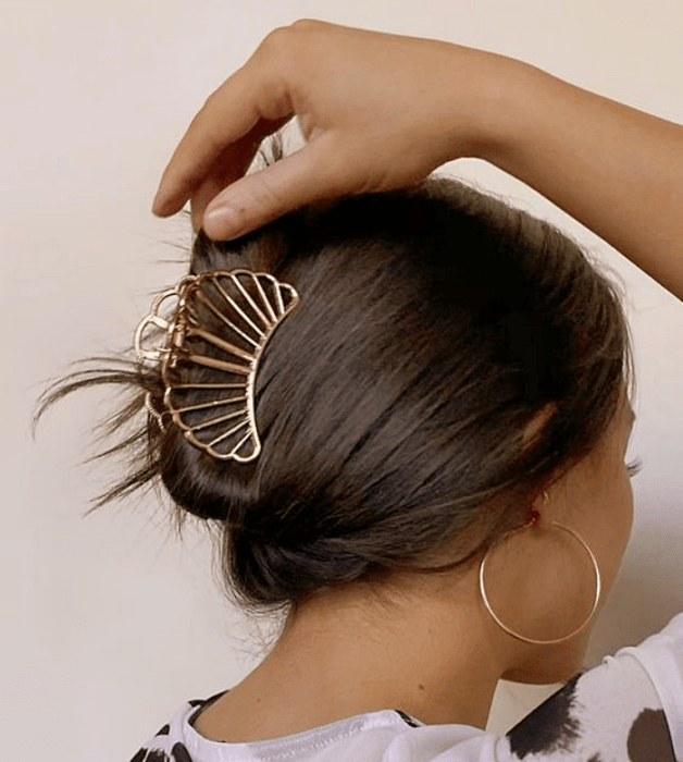 chica de cabello castaño usando una pinza para el cabello de metal en forma de coral, blusa blanca con negro