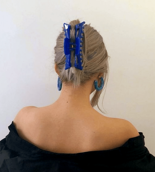 chica rubia platinada con pinza para el cabello azul, blusa negra de hombros caídos