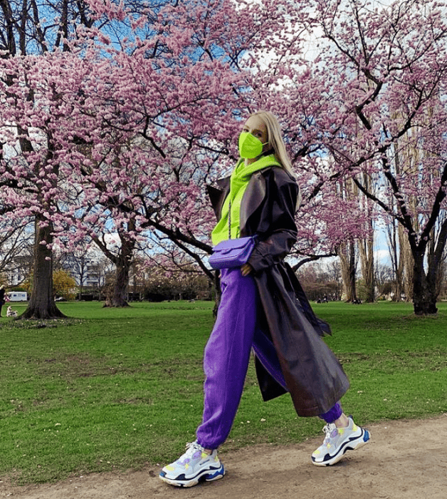 chica rubia con bufanda verde limón, pants morados, tenis blancos con morado, abrigo largo café oscuro