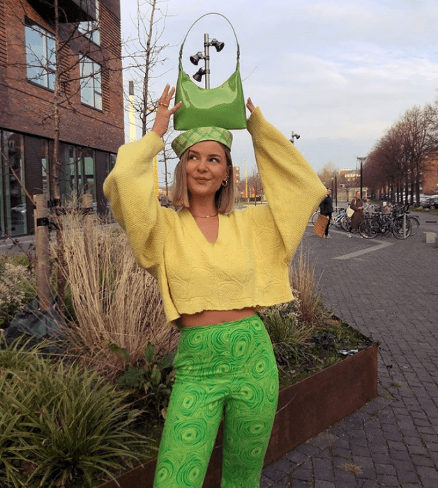 chica rubia con bolso verde pequeño, suéter amarillo holgado, leggings pantalones verdes brillantes