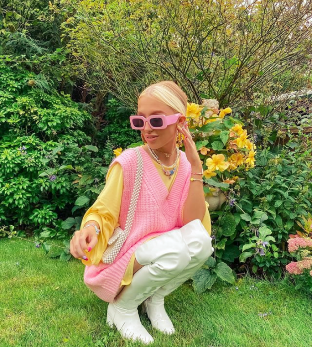 chica rubia con lentes de sol rosas, suéter rosa con mangas amarillas, botas largas blancas de cuero con tacón, bolso rosa de cuero