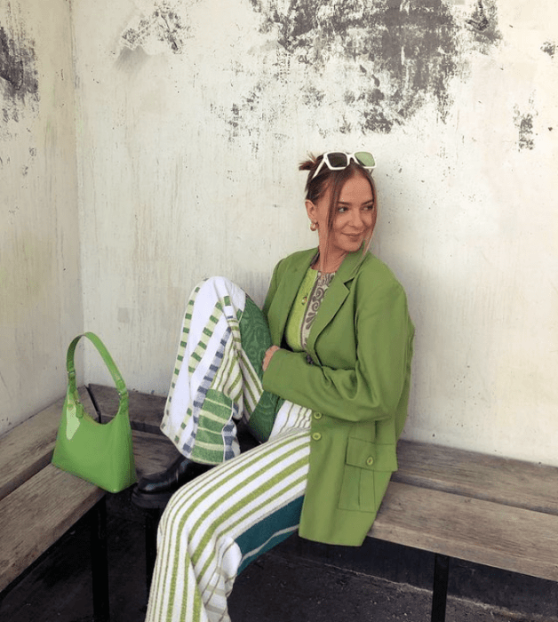 chica de cabello oscuro usando lentes de sol verdes, blazer verde holgado, top verde limón, pantalones blancos con líneas verdes, bolso verde de cuero