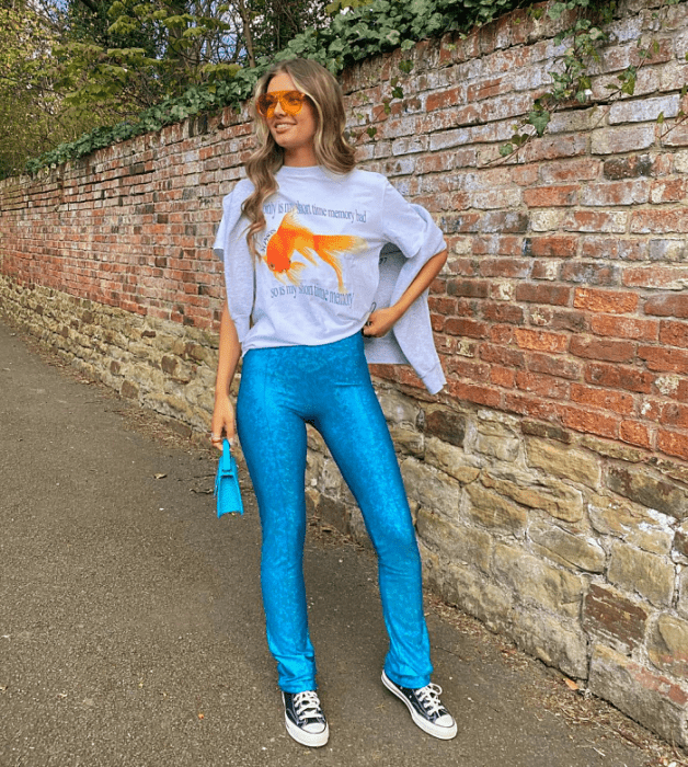 chica de cabello claro con lentes de sol naranja, camiseta blanca gráfica, pantalones azul brillante, tenis converse negros, bolso pequeño celeste