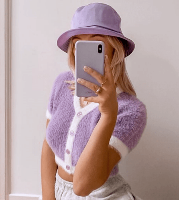 chica de cabello rubio con bucket hat lila, suéter de manga corta lila con borde blanco y pantalones blancos a la cintura