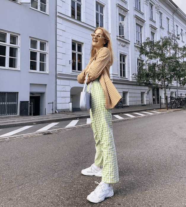 chica rubia con lentes de sol beige, blazer amarillo con cuadros blancos, pantalones verdes claros, tenis blancos, bolso lila