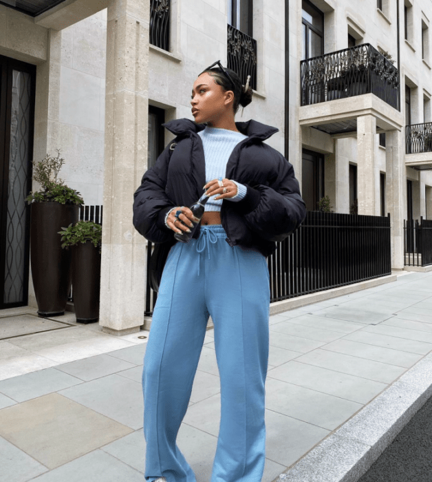 chica morena usando un crop top celeste, chamarra negra puffer, pants celestes holgados