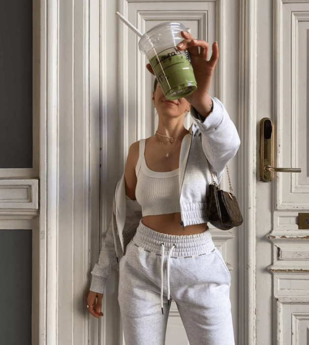 chica usando un crop top blanco de tirantes, sudadera blanca de zipper, pants blancos, bolso pequeño café