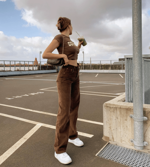 chica de cabello castaño usando un crop top café, cubrebocas negro, camisa de cuadros oversized café con negro y beige, jeans ajustados a la cintura