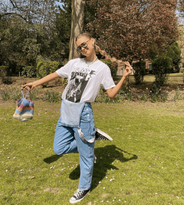 chica rubia con lentes de sol, camiseta blanca oversized, overol de mezclilla holgado, tenis deportivos converse negros