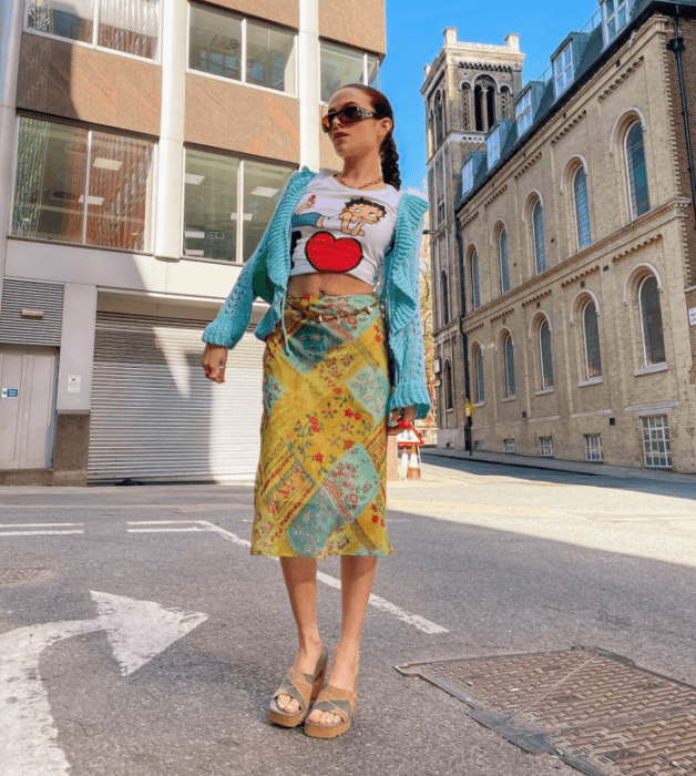 chica de cabello oscuro usando lentes de sol, camiseta gráfica blanca con corazón rojo, falda amarilla con verde y azul, sandalias de plataforma café