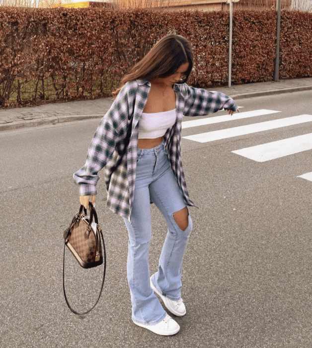 chica de cabello castaño usando un crop top blanco, camisa de cuadros holgada, tenis acampanados rotos, tenis blancos y bolso café de piel