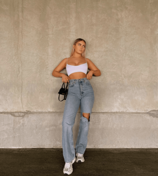 chica rubia con crop top de tirantes, jeans holgados rotos, tenis blancos, bolso pequeño negro