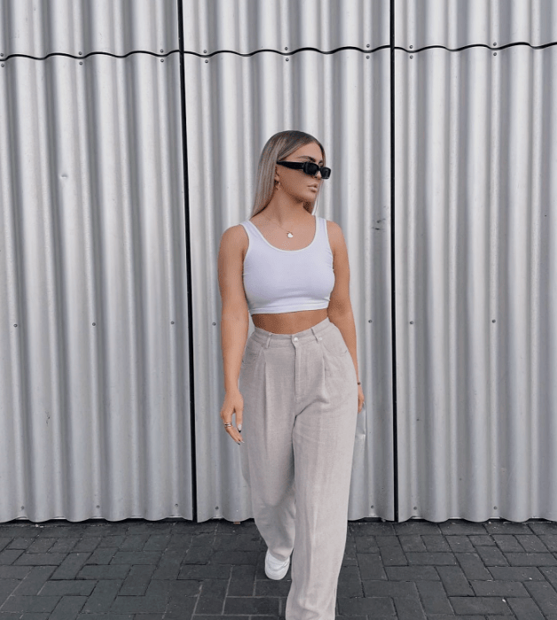 chica rubia con lentes de sol, crop top blanco de tirantes, pantalones beige claros holgados de vestir