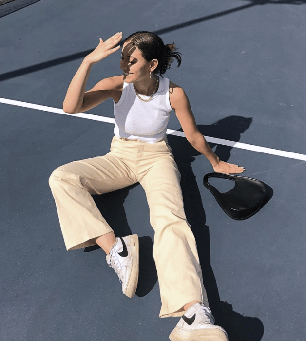 chica de cabello oscuro usando un top blanco halter, pantalones beige claros holgados, tenis blancos con negro, bolso pequeño negro de cuero