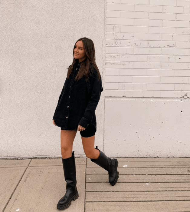 chica de cabello castaño con camisa negra oversized, biker shorts de ciclismo negros, botas largas de cuero