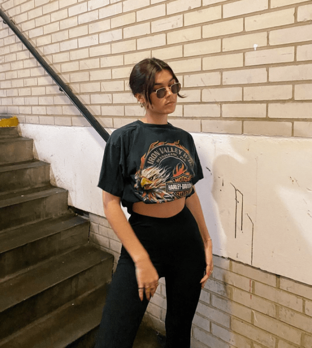 chica de cabello castaño usando lentes de sol, camiseta negra de banda de rock, leggings negros de tiro alto