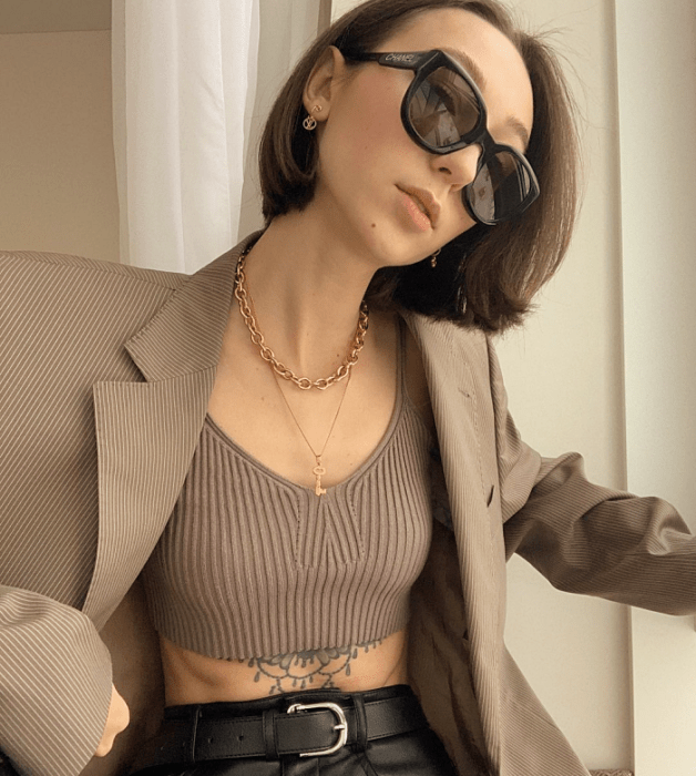 chica de cabello castaño corto usando lentes de sol, crop top café tejido, saco blazer café claro holgado, pantalones de cuero ajustados a la cintura