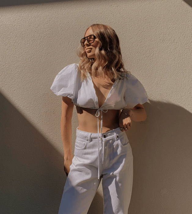 chica rubia con lentes de sol, crop top blanco de manga corta, jeans ajustados blancos