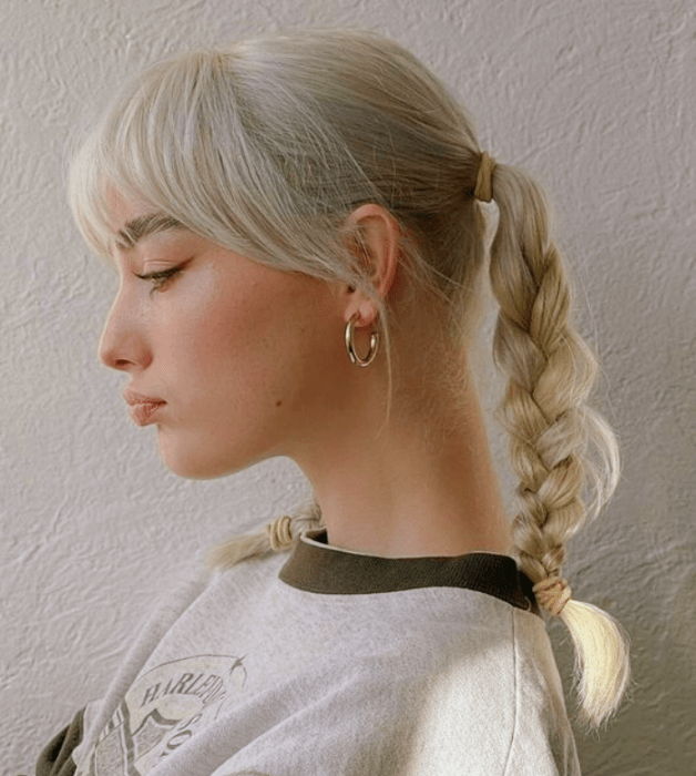 chica de cabello platinado usando coletas con trenzas, playera blanca con cuello verde militar