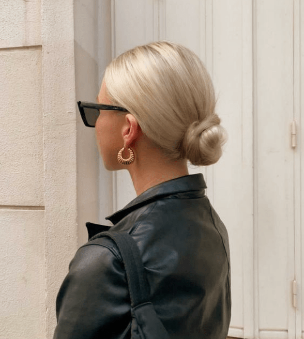 chica de cabello platinado con chongo bajo, lentes de sol negros y chamarra de cuero negro 