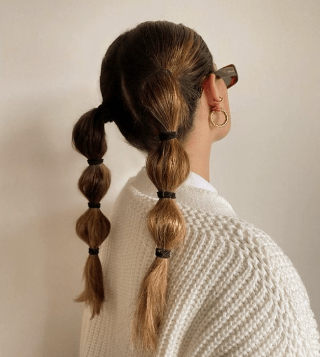 chica de cabello claro largo usando coletas abombadas con suéter blanco y lentes de sol negros