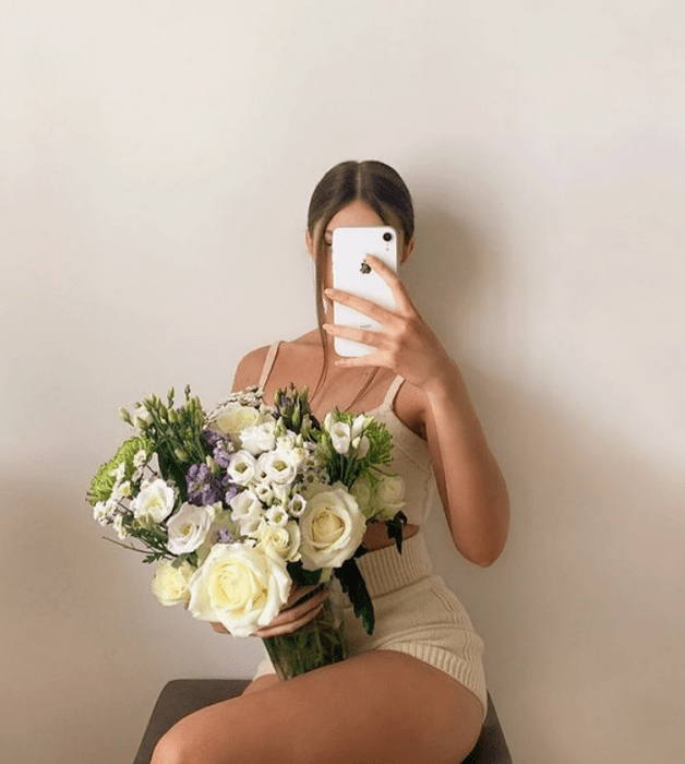 chica de cabello castaño usando un top de tirantes tejido beige, shorts tejidos beige y un florero en la mano