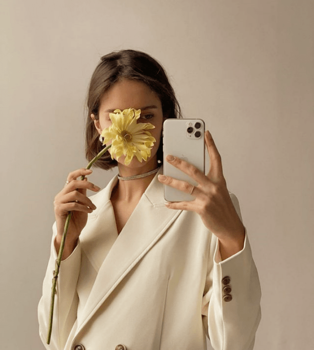 chica de cabello castaño corto usando un blazer saco beige grande con flor amarilla en la mano cubriéndole el rostro