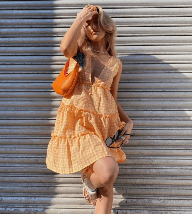 chica rubia con vestido naranja holgado con vuelo, bolso naranja brillante de cuero pequeño y tenis blancos con naranja